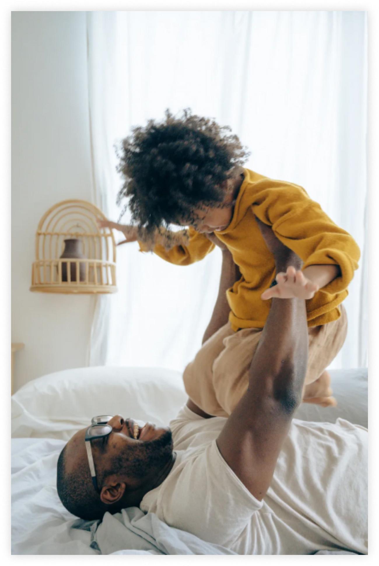 Dad lifting young child up while laying in bed