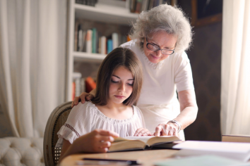 Older mom helping her teenage daughter with reading